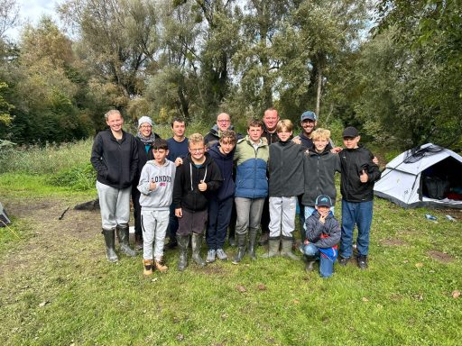 Gruppe von Personen in Gummistiefeln, lächelnd im Freien, umgeben von Bäumen und Zelten.